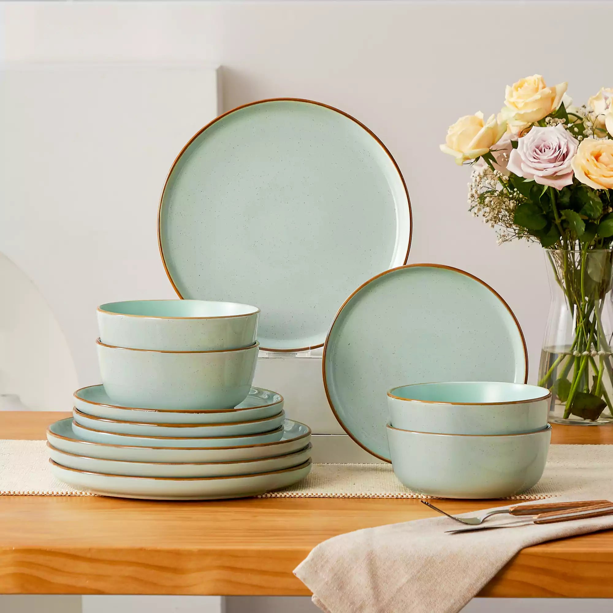 Green rustic stoneware dinnerware set with speckled - lipped-edge plates and bowls on a dining table with flowers and cutlery in a cozy modern kitchen-vancasso