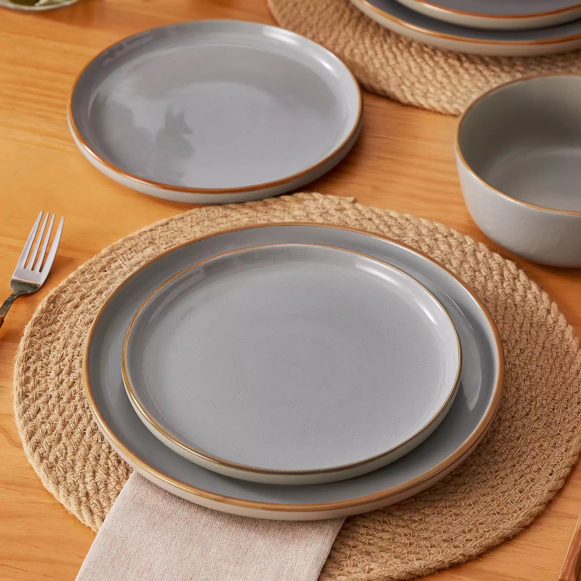 Grey rustic stoneware dinnerware set with speckled - lipped-edge plates and bowls on a dining table with flowers and cutlery in a cozy modern kitchen-vancasso
