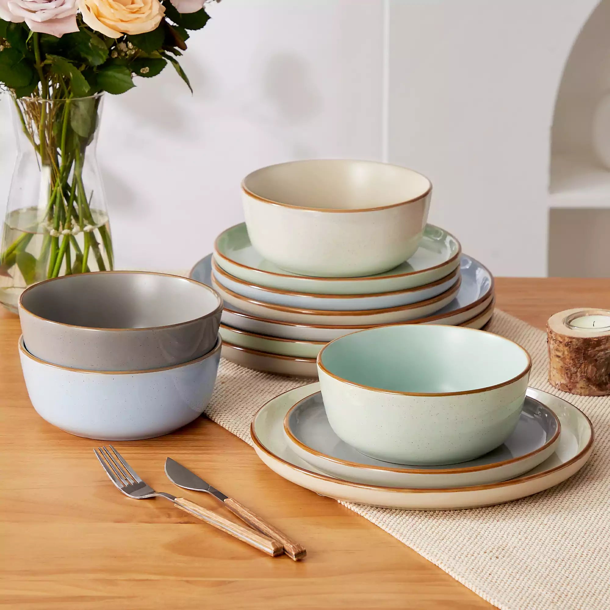 Assorted rustic stoneware dinnerware set with speckled - lipped-edge plates and bowls on a dining table with flowers and cutlery in a cozy modern kitchen-vancasso