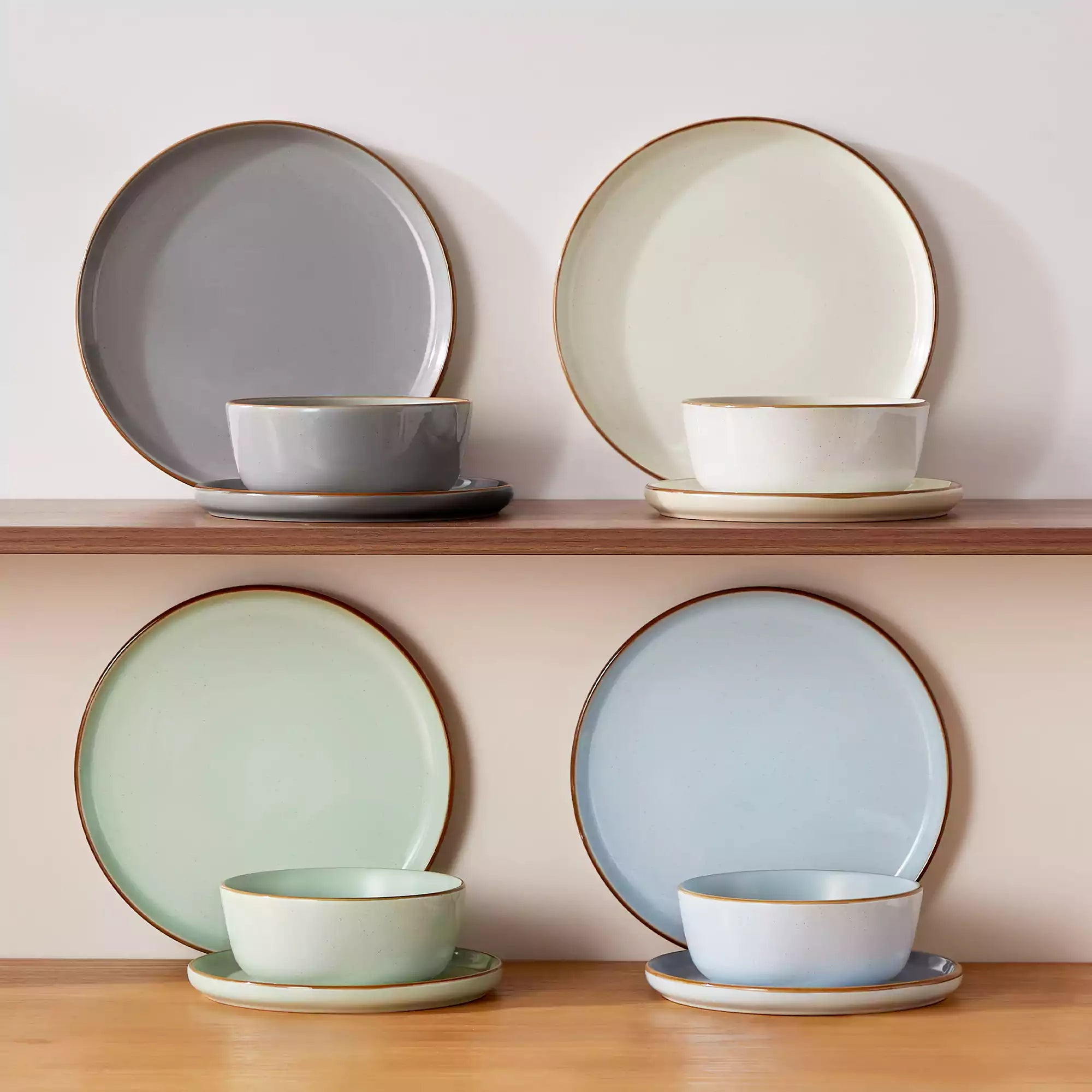 Assorted rustic stoneware dinnerware set with speckled - lipped-edge plates and bowls on a dining table with flowers and cutlery in a cozy modern kitchen-vancasso