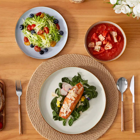 Assorted rustic stoneware dinnerware set with speckled - lipped-edge plates and bowls on a dining table with flowers and cutlery in a cozy modern kitchen-vancasso