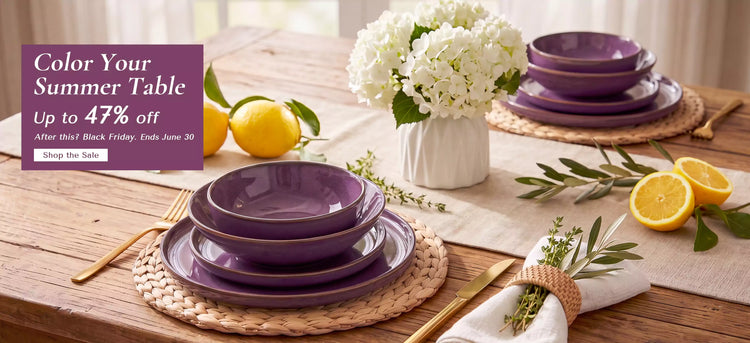 Purple Sata stoneware dinnerware set for 6 featuring lipped edge plates and bowls with reactive glaze styled on a wooden dining table with white hydrangeas and fresh lemons