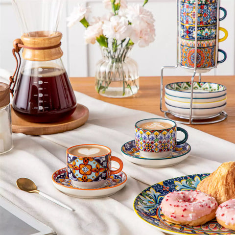 Simi 12 piece porcelain espresso set with 3oz cups and saucers in vibrant boho chic floral patterns on a black metal storage rack with a magazine and napkin on a wooden table