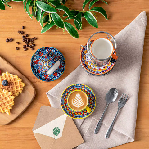 Simi 12 piece porcelain espresso set with 3oz cups and saucers in vibrant boho chic floral patterns on a black metal storage rack with a magazine and napkin on a wooden table