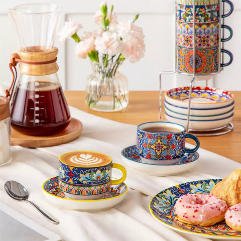 Simi 12 piece porcelain cafe set with 5oz flat white cups and saucers in vibrant boho chic floral patterns on a black metal storage rack with a magazine and napkin on a wooden table