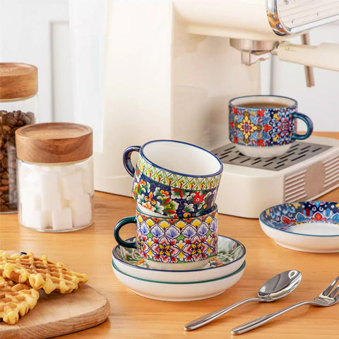 Simi 12 piece porcelain cafe set with 5oz flat white cups and saucers in vibrant boho chic floral patterns on a black metal storage rack with a magazine and napkin on a wooden table