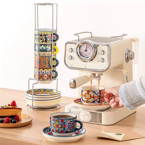 Simi 12 piece porcelain cafe set with 9oz flat white cups and saucers in vibrant boho chic floral patterns on a black metal storage rack with a magazine and napkin on a wooden table