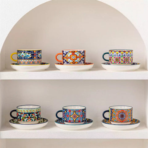 Simi 12 piece porcelain cafe set with 9oz flat white cups and saucers in vibrant boho chic floral patterns on a black metal storage rack with a magazine and napkin on a wooden table