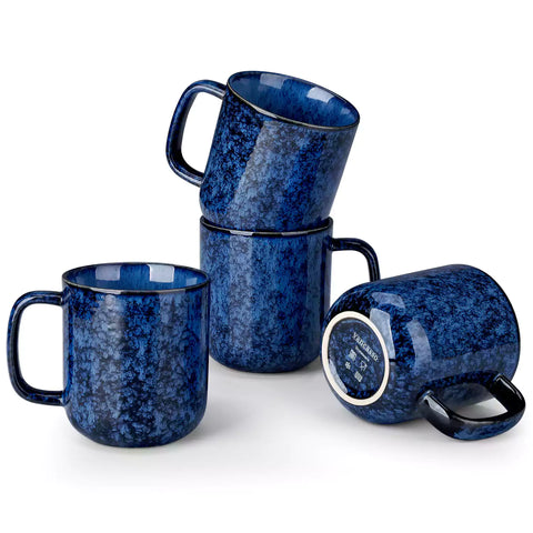 Four starry blue 16oz stoneware mugs with latte art on wooden table beside coffee brewing equipment
