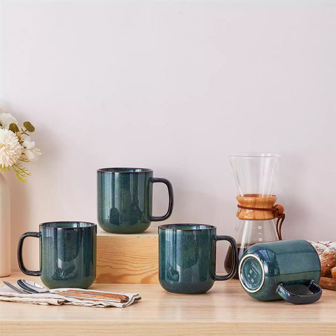 Four starry green 16oz stoneware mugs with latte art on wooden table beside coffee brewing equipment