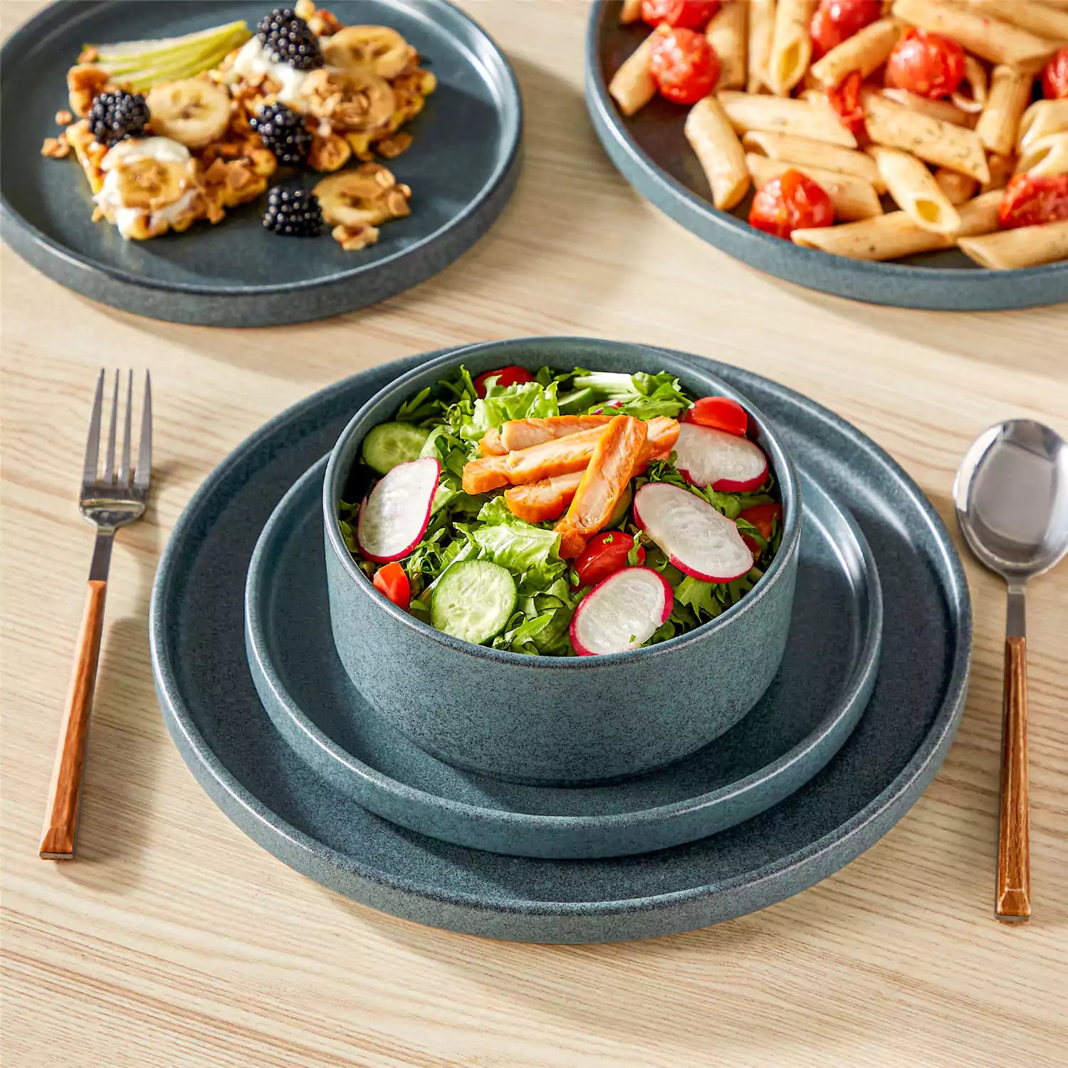 Blue reactive glaze stoneware dinner plates styled with food on rustic wood table with woven placemats modern minimalist tableware set