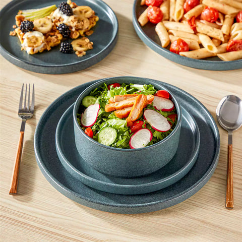 Blue reactive glaze stoneware dinner plates styled with food on rustic wood table with woven placemats modern minimalist tableware set