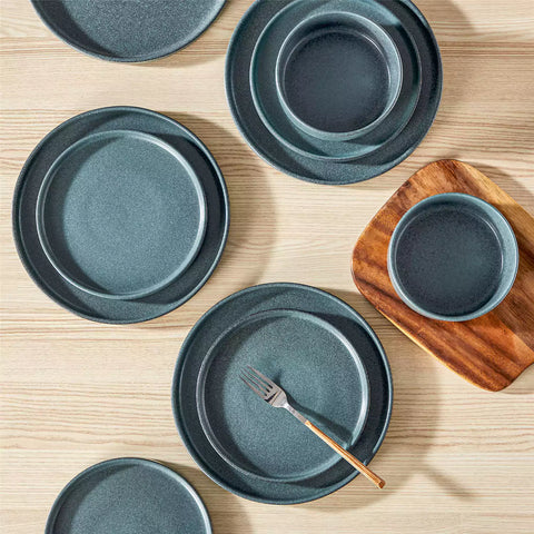 Blue reactive glaze stoneware dinner plates styled with food on rustic wood table with woven placemats modern minimalist tableware set
