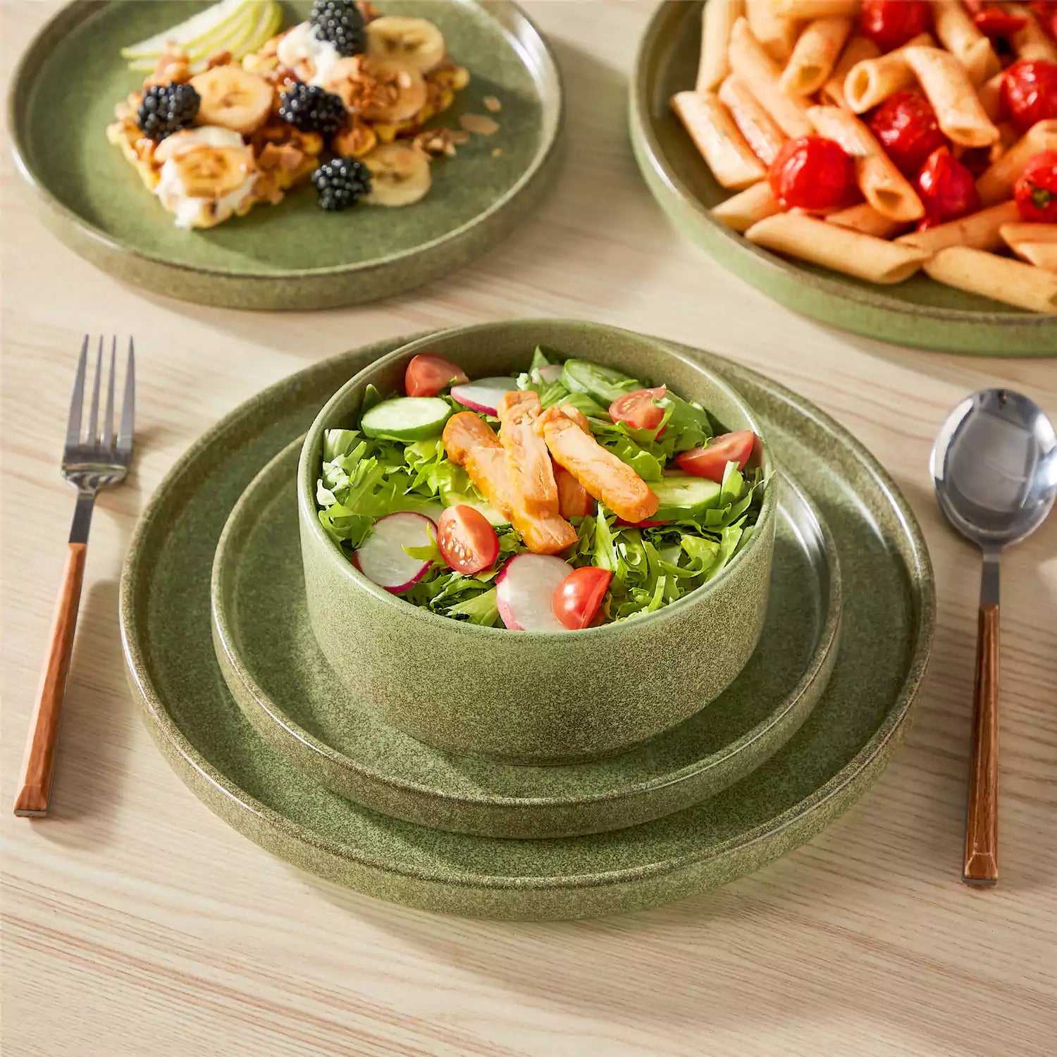 Green reactive glaze stoneware dinner plates styled with food on rustic wood table with woven placemats modern minimalist tableware set