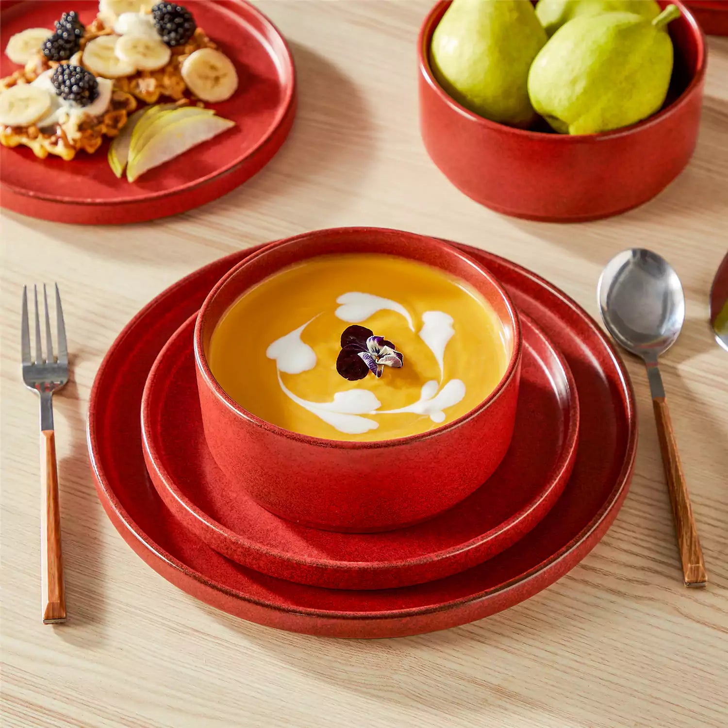 Red reactive glaze stoneware dinner plates styled with food on rustic wood table with woven placemats modern minimalist tableware set