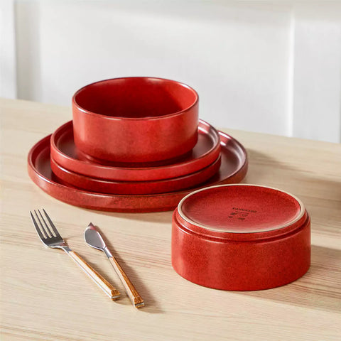 Red reactive glaze stoneware dinner plates styled with food on rustic wood table with woven placemats modern minimalist tableware set