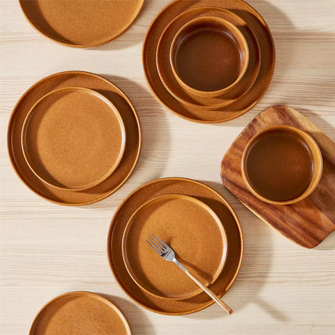 Caramel reactive glaze stoneware dinner plates styled with food on rustic wood table with woven placemats modern minimalist tableware set